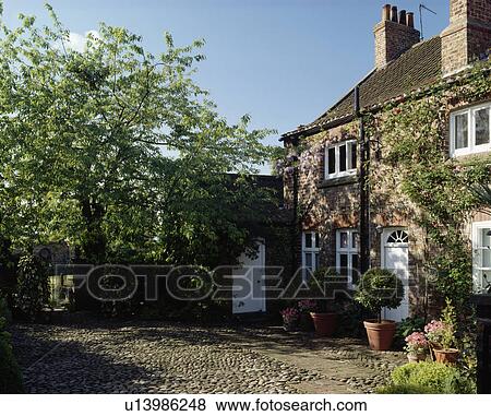 Stock Photo - Pebble and stone paving on courtyard in front of traditional country cottage. Fotosearch
