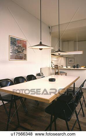 Stock Photo - Pendant lamps above rectangular modern table with black chairs in white eighties dining room. Fotosearch