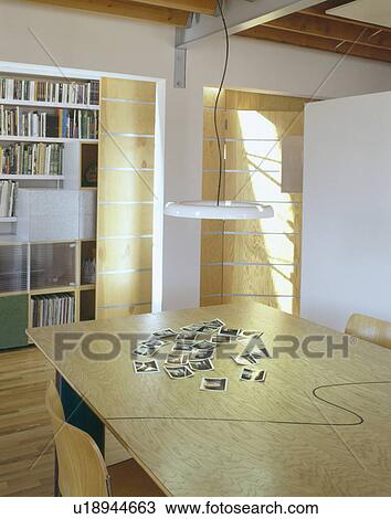 Pendant light above black and white photographs on light wood table in modern city dining room View Large Photo Image Stock Image - Pendant light above black and white photographs on light wood table in modern city dining room. Fotosearch