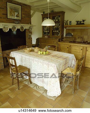 Pendant light above rectangular table with long white cloth in country dining room with rush-seated chairs and tiled floor View Large Photo Image Stock Photo - Pendant light above rectangular table with long white cloth in country dining room with rush-seated chairs and tiled floor. Fotosearch