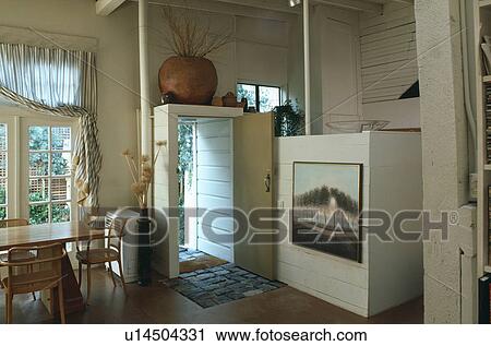 Stock Image - Picture on wall of dining room in converted garage with table and chairs beside open door. Fotosearch