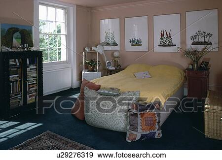 Pictures above bed with yellow duvet in sixties bedroom with large floor cushions View Large Photo Image Stock Photo - Pictures above bed with yellow duvet in sixties bedroom with large floor cushions. Fotosearch
