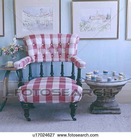 Stock Photo - Pictures above red & white checked upholstered Victorian chair and glass topped stone table . Fotosearch