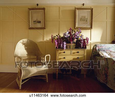 Pictures on cream panelled walls of country bedroom with wicker armchair and flowers on small antique table View Large Photo Image Picture - Pictures on cream panelled walls of country bedroom with wicker armchair and flowers on small antique table. Fotosearch