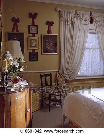 Pictures on ribbon bows on wall in traditional bedroowm with white curtains and nets on window View Large Photo Image Stock Image - Pictures on ribbon bows on wall in traditional bedroowm with white curtains and nets on window. Fotosearch