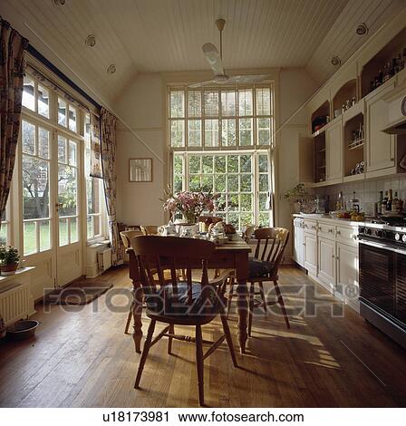 Stock Image - Pine chairs and table in traditional kitchen with wooden flooring and large windows. Fotosearch