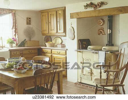 Stock Image - Pine table and chairs in country kitchen with cream Aga. Fotosearch