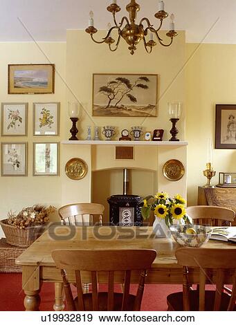 Stock Photo - Pine table and chairs in pastel yellow country dining room with black stove in fireplace. Fotosearch