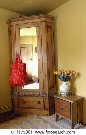 Stock Image - Pine wardrobe with mirrored door beside small cupboard in corner of yellow bedroom. Fotosearch