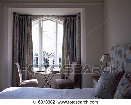 Pink chairs and small metal table in front of window with pale grey curtains in small bedroom View Large Photo Image Stock Image - Pink chairs and small metal table in front of window with pale grey curtains in small bedroom. Fotosearch