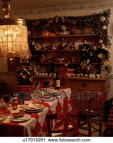 Stock Image - Place settings on red+white patchwork tablecloth in dining room with dresser decorated for Christmas. Fotosearch