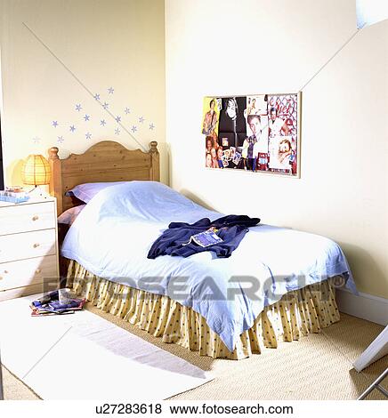 Stock Photo - Pop group poster above pine bed with blue duvet and yellow vallance in teenager's bedroom with blue stars above bed&#13; &#10; &#13; &#10; &#13; &#10; &#13; &#10; &#13; &#10; &#13; &#10;. Fotosearch