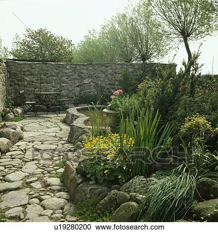 Stock Image - Raised pond and green plants in summer country garden. Fotosearch