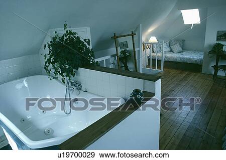Raised spa bath in white attic ensuite bathroom with wooden flooring View Large Photo Image Stock Photo - Raised spa bath in white attic ensuite bathroom with wooden flooring. Fotosearch