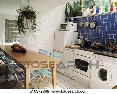 Row of domestic appliances below blue wall tiles in small basement kitchen tall mirror and with wooden table View Large Photo Image Stock Photo - Row of domestic appliances below blue wall tiles in small basement kitchen tall mirror and with wooden table . Fotosearch