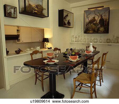Picture - Rush-seated chairs and pedestal table in white dining room with stuffed birds in glass cases on wall. Fotosearch