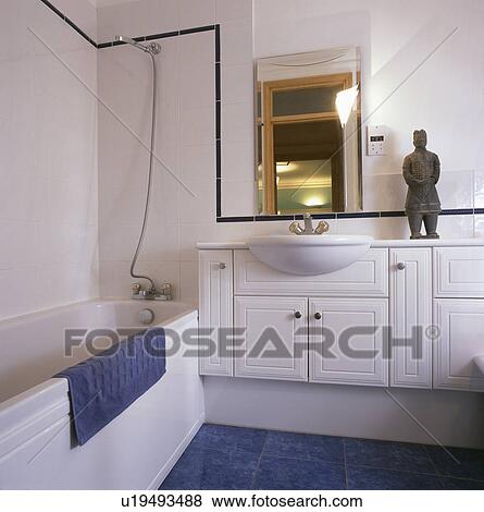 Stock Photo - Sculpture on white fitted vanit unit with white basin in modern white bathroom with shower above bath. Fotosearch