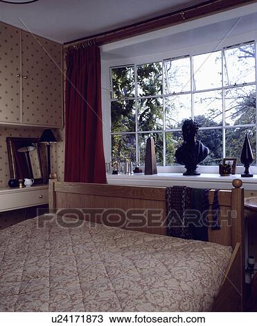 Stock Image - Sculpture on windowsill in bedroom with patterned beige quilt. Fotosearch