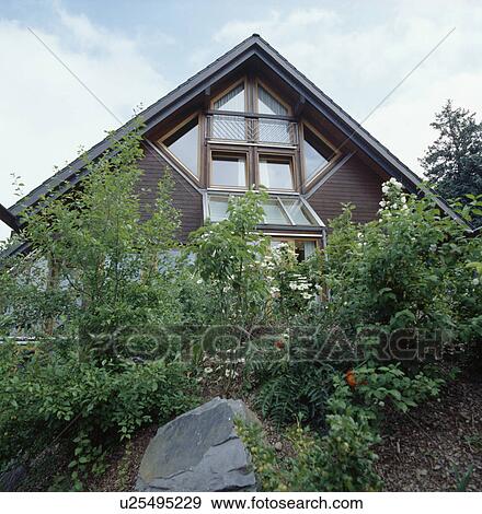 Stock Photo - Shrubs in front of modern German house with apex roof. Fotosearch