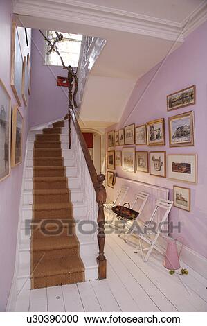 Stock Image - Sisal carpet on white staircase in mauve hall with white wooden floor and picture above white folding chairs. Fotosearch