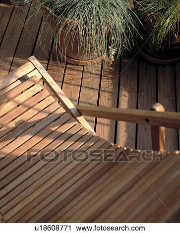 Stock Image -  Slatted deckchair on sunny decking with pots of grasses. &#13; &#10;. Fotosearch