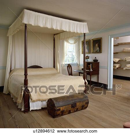 Small antique wooden chest in front of four-poster bed with cream bedcover in colonial-style bedroom with wooden floor View Large Photo Image Stock Image - Small antique wooden chest in front of four-poster bed with cream bedcover in colonial-style bedroom with wooden floor. Fotosearch