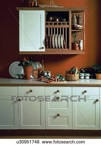 Stock Photo - Small cupboard and plate rack in traditional terracotta kitchen with white fitted cupboards. Fotosearch