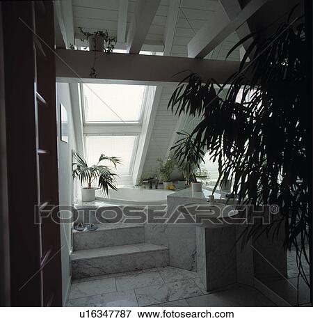 Stock Photo - Small mirrored white bathroom with marble tiled steps leading to sunk bath in the eaves of a modern attic conversion. Fotosearch