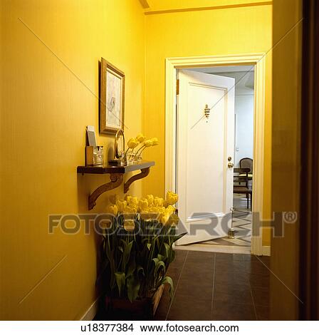 Picture - Small shelf above yellow tulips in bright yellow hall with white door. Fotosearch
