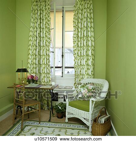 Small table and chair in front of window with green curtains in bright green study with white wicker armchair View Large Photo Image Stock Photo - Small table and chair in front of window with green curtains in bright green study with white wicker armchair. Fotosearch