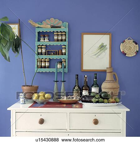Stock Photo - Small turquoise wooden shelves above white chest of draers with bottles of wine and bowls of fruit. Fotosearch
