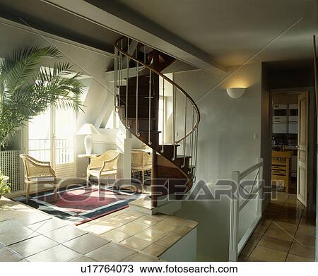 Stock Image - Spiral staircase and wicker chairs on tiled floor in openplan landing . Fotosearch