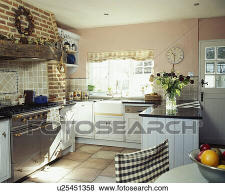 Stock Photo - Stainless steel range oven in country kitchen with white painted fitted cupboards. Fotosearch
