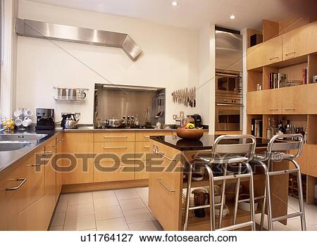 Stainless steel stools at island unit in modern kitchen with pale wood fitted cupboards View Large Photo Image Stock Photo - Stainless steel stools at island unit in modern kitchen with pale wood fitted cupboards . Fotosearch