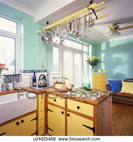 Steel utensils on wooden ceiling rack in turquoise kitchen with ceramic sink and yellow doors on fitted cupboards View Large Photo Image Stock Photo - Steel utensils on wooden ceiling rack in turquoise kitchen with ceramic sink and yellow doors on fitted cupboards. Fotosearch