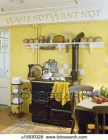Stock Photo - Stencilled graffiti text above terracotta pots and black Aga in traditional yellow kitchen with pans on freestanding rack. Fotosearch