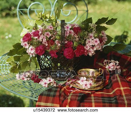 Stock Image - Still-life of red dianthus and pink roses in floral arrangement with antique cup. Fotosearch