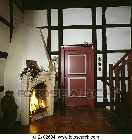 Stone mantelpiece on corner fireplace with lighted fire in country hall with black beams and red door View Large Photo Image Picture - Stone mantelpiece on corner fireplace with lighted fire in country hall with black beams and red door. Fotosearch