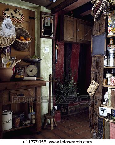 Stock Photography - Storage baskets on wall above scales on old table in dark cottage kitchen. Fotosearch