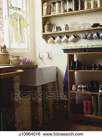 Storage jars on wall shelves above white sink in utility room with boots and shoes stored on freestanding wooden shelf unit View Large Photo Image Stock Photograph - Storage jars on wall shelves above white sink in utility room with boots and shoes stored on freestanding wooden shelf unit. Fotosearch