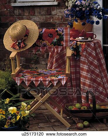 Stock Image - Straw hat on floral directors chair in front of table with red checked cloth. Fotosearch
