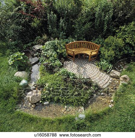 Stock Photo - Stream flowing around patio with curved wooden bench in country garden. Fotosearch