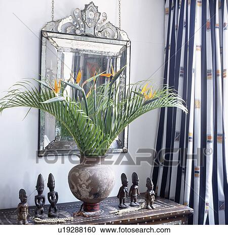 Strelitzia and green palm leaves in ethnic with collection of small African figures on inlaid cupboard below antique Venetian mirror View Large Photo Image Stock Image - Strelitzia and green palm leaves in ethnic with collection of small African figures on inlaid cupboard below antique Venetian mirror. Fotosearch