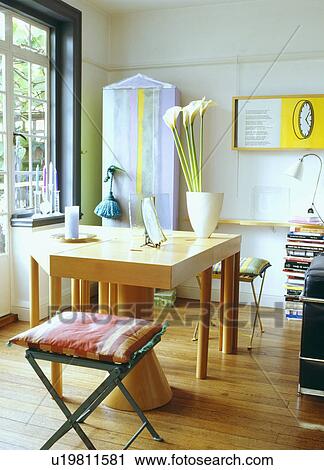 Stock Image - Striped cushions on metal stools in modern dining room with pale wood table and wooden flooring. Fotosearch