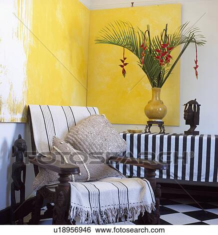Striped throw on wooden armchair in corner of living room below large yellow abstract double painting View Large Photo Image Stock Photograph - Striped throw on wooden armchair in corner of living room below large yellow abstract double painting . Fotosearch