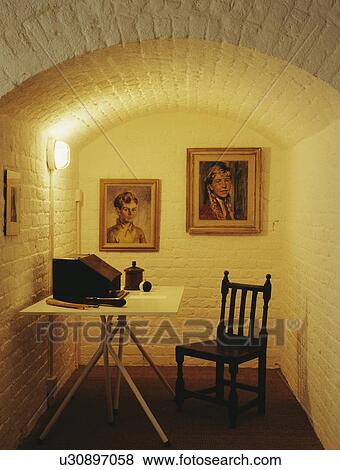 Stock Photo - Table and chair in basement study with pictures on wall. Fotosearch