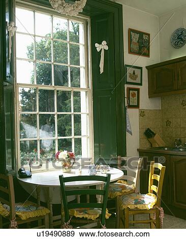 Stock Photo - Table and chairs in front of sash window with green shutters in country dining room. Fotosearch