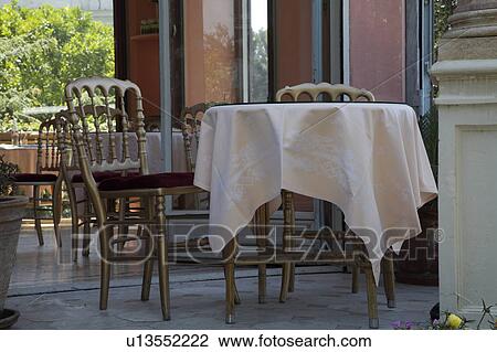 Stock Image - Table with white cloth and gilt chairs outside restaurant in Paris. Fotosearch