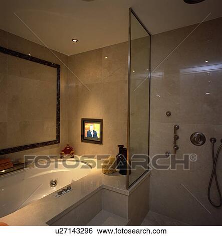 Stock Photograph - Television set into marble tiled wall above bath in modern bathroom with open shower. Fotosearch