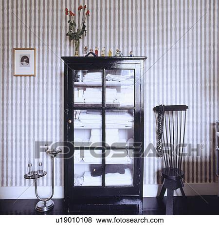 Towels stored in glass fronted black cupboard in bathroom with black chair and black & white striped wallpaper View Large Photo Image Stock Photo - Towels stored in glass fronted black cupboard in bathroom with black chair and black & white striped wallpaper. Fotosearch
